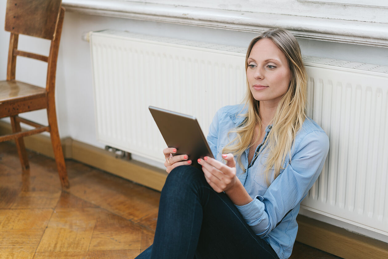 Frau mit Tablet vor Heizung